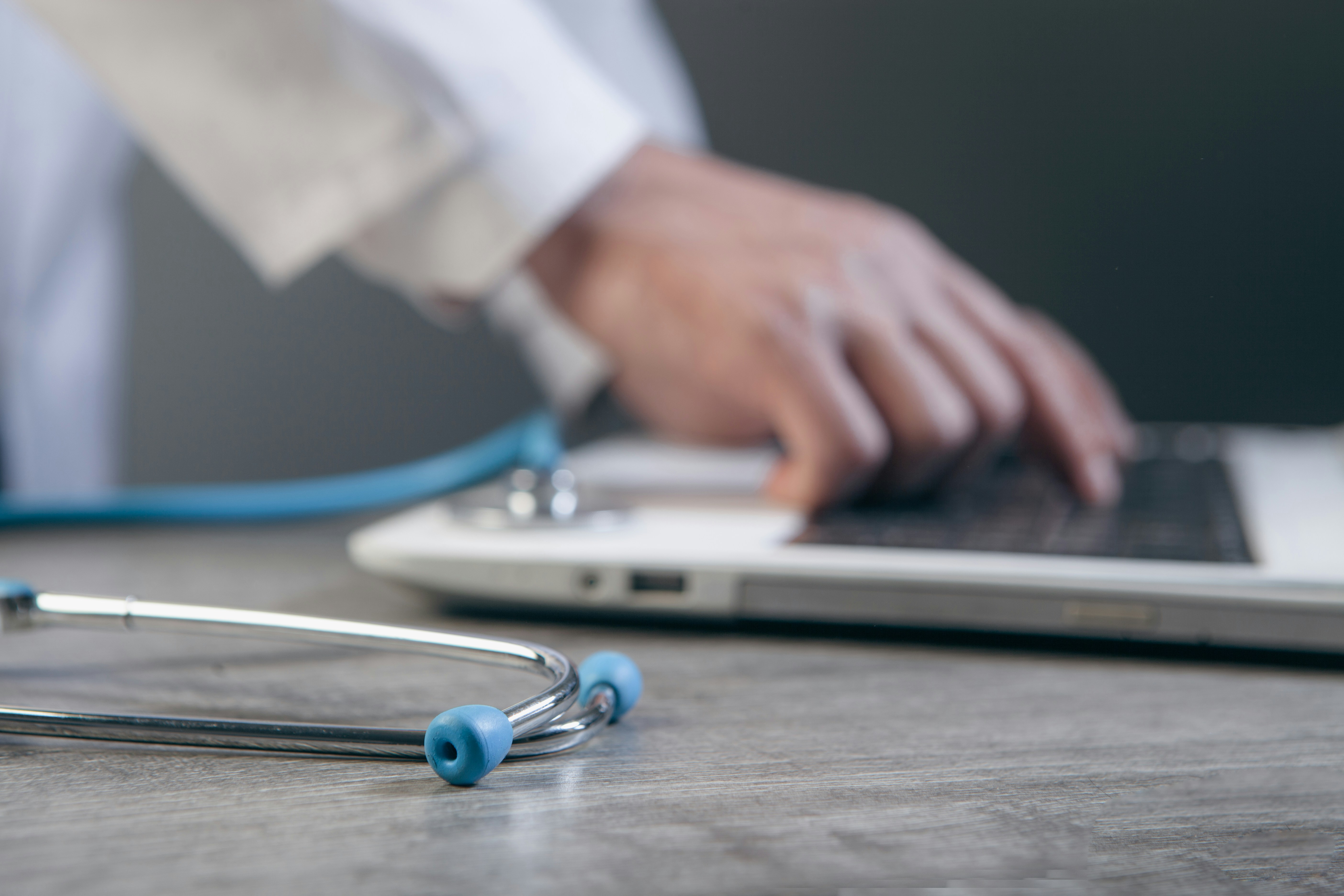 Close-up of a healthcare professional using a laptop with a stethoscope on a desk.