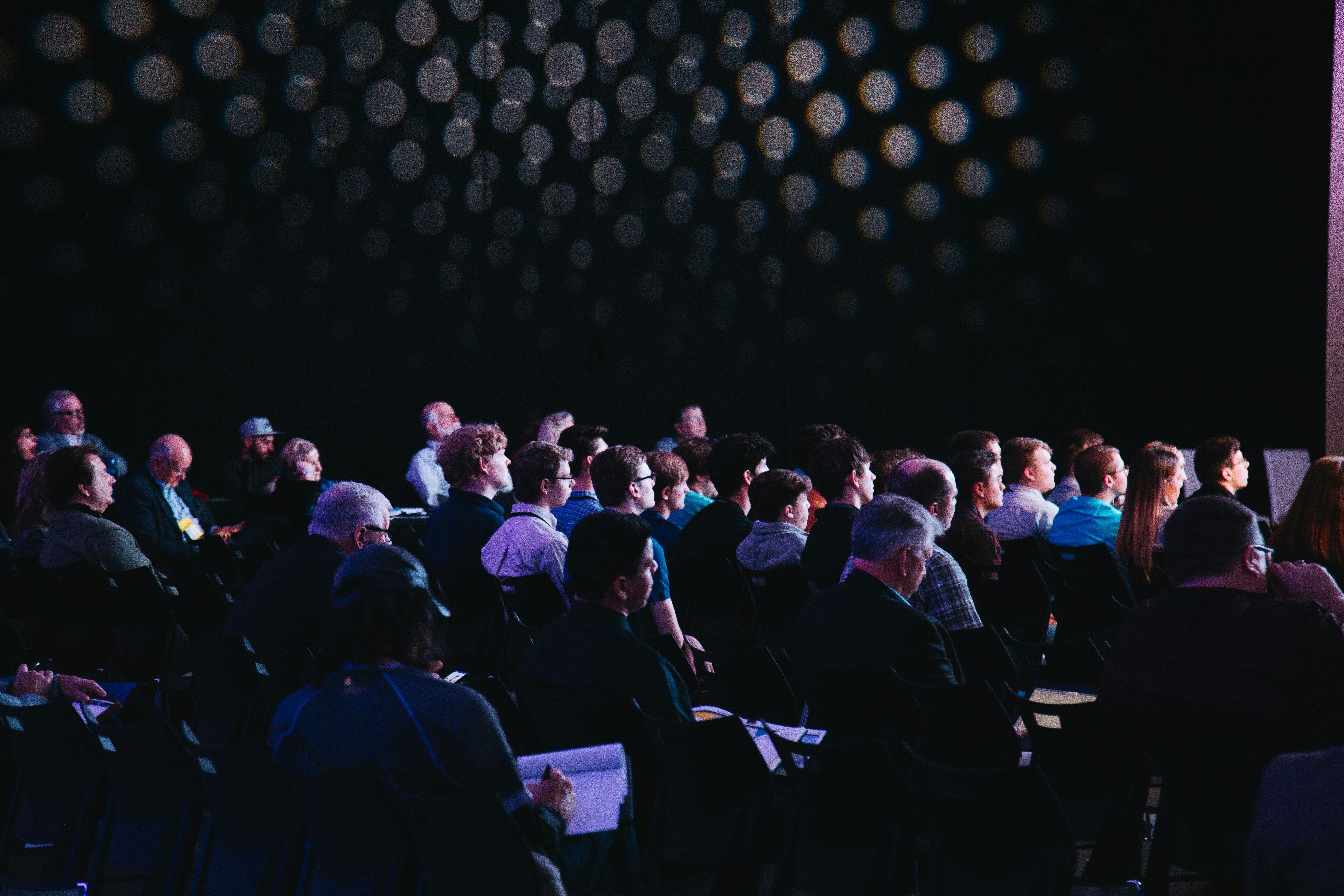 Audience members seated in a conference session facing a presentation stage.